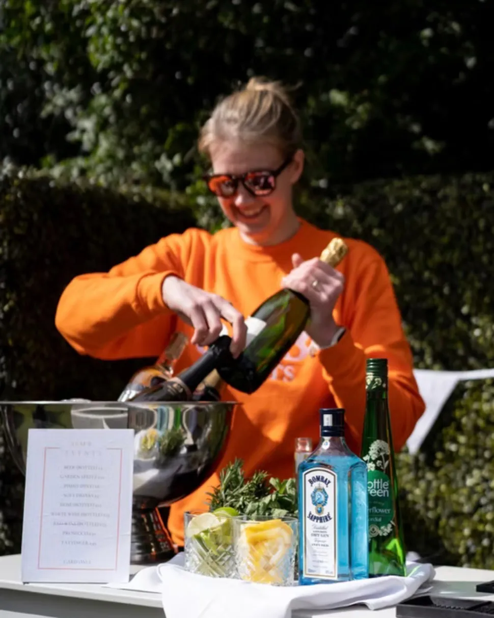 Maxi Level opening a bottle at a drinks table set up outside