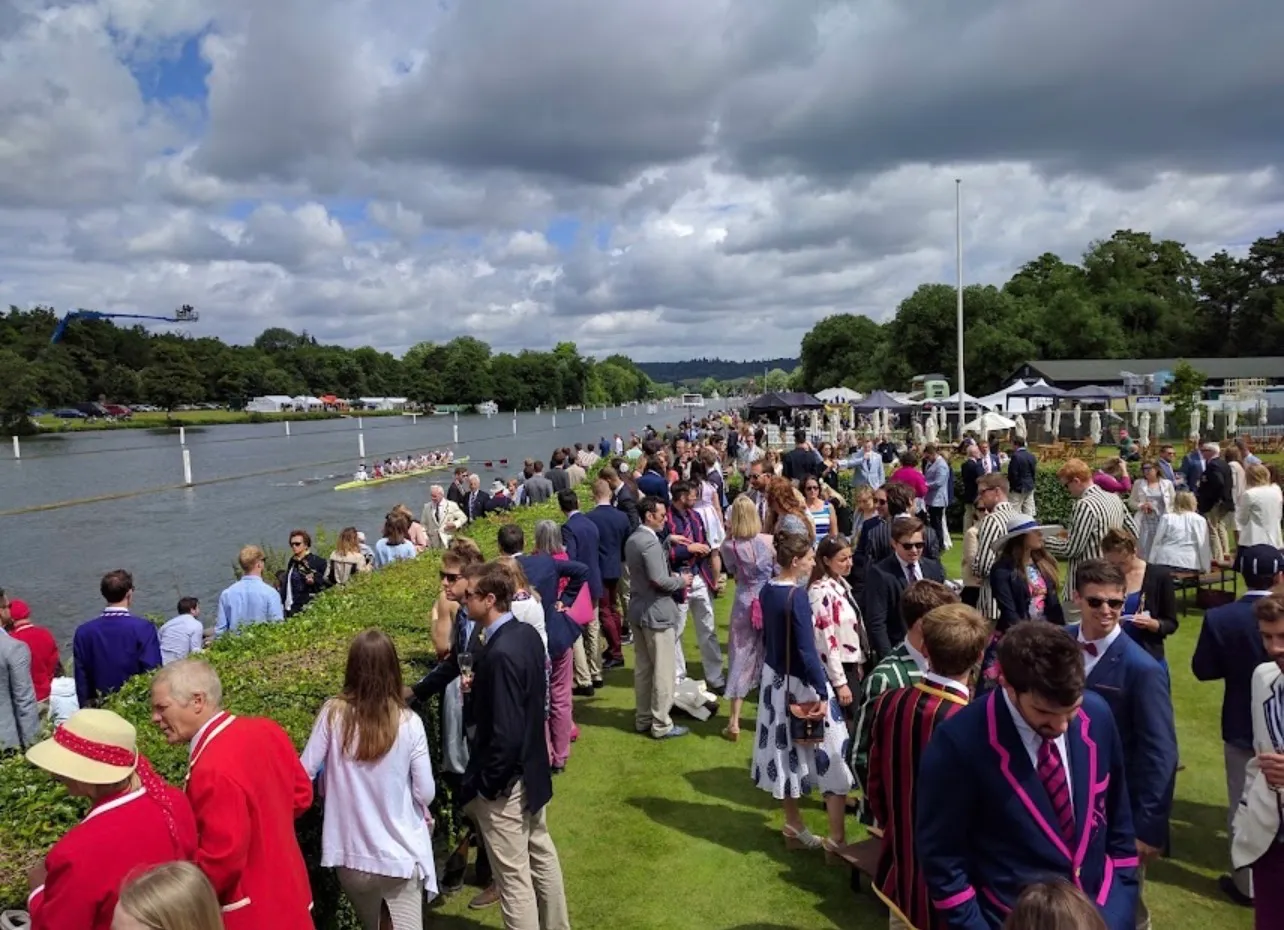 Guests the length of the bank during the regatta, a crew racing on the water beyond them