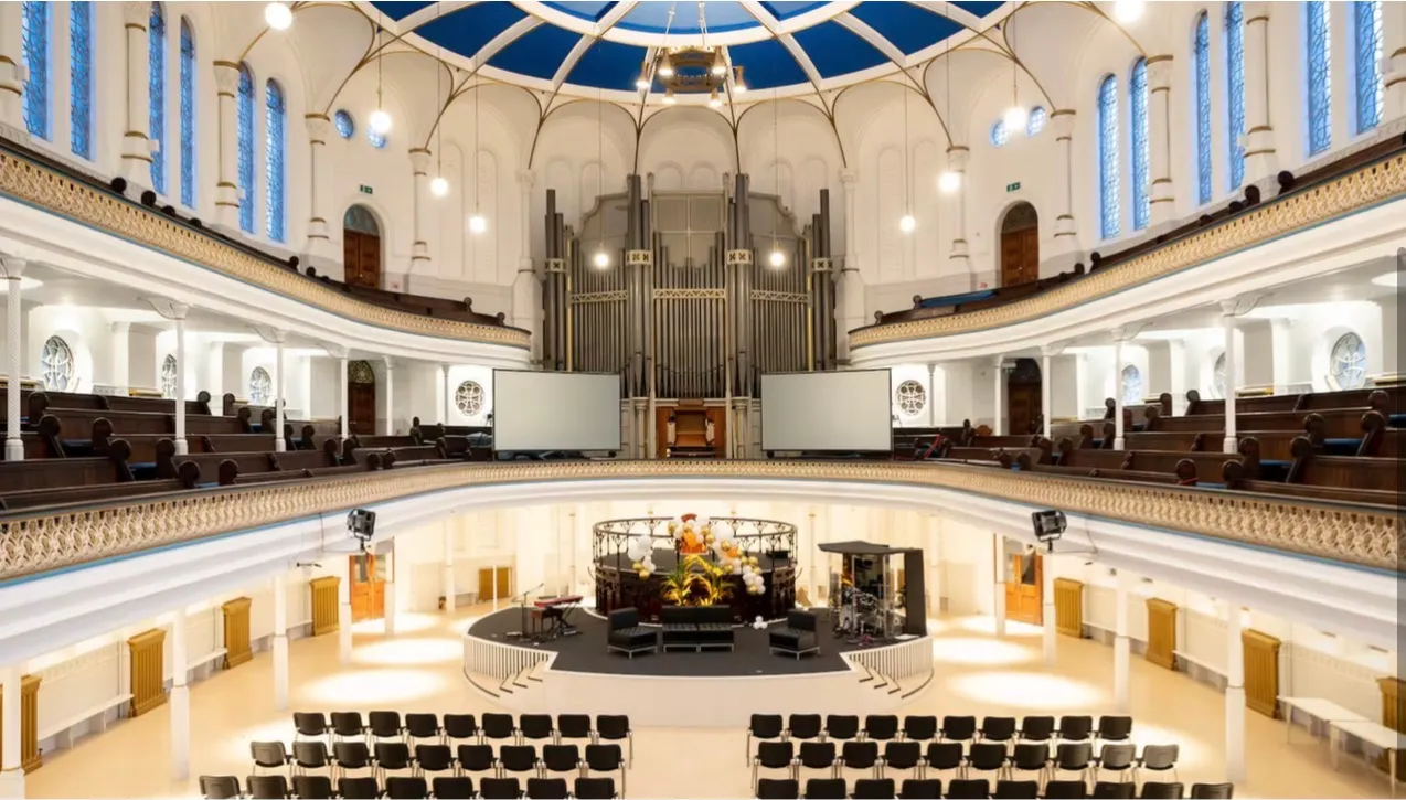 A galleried chapel auditorium from the upper level, seating laid out below the organ pipes