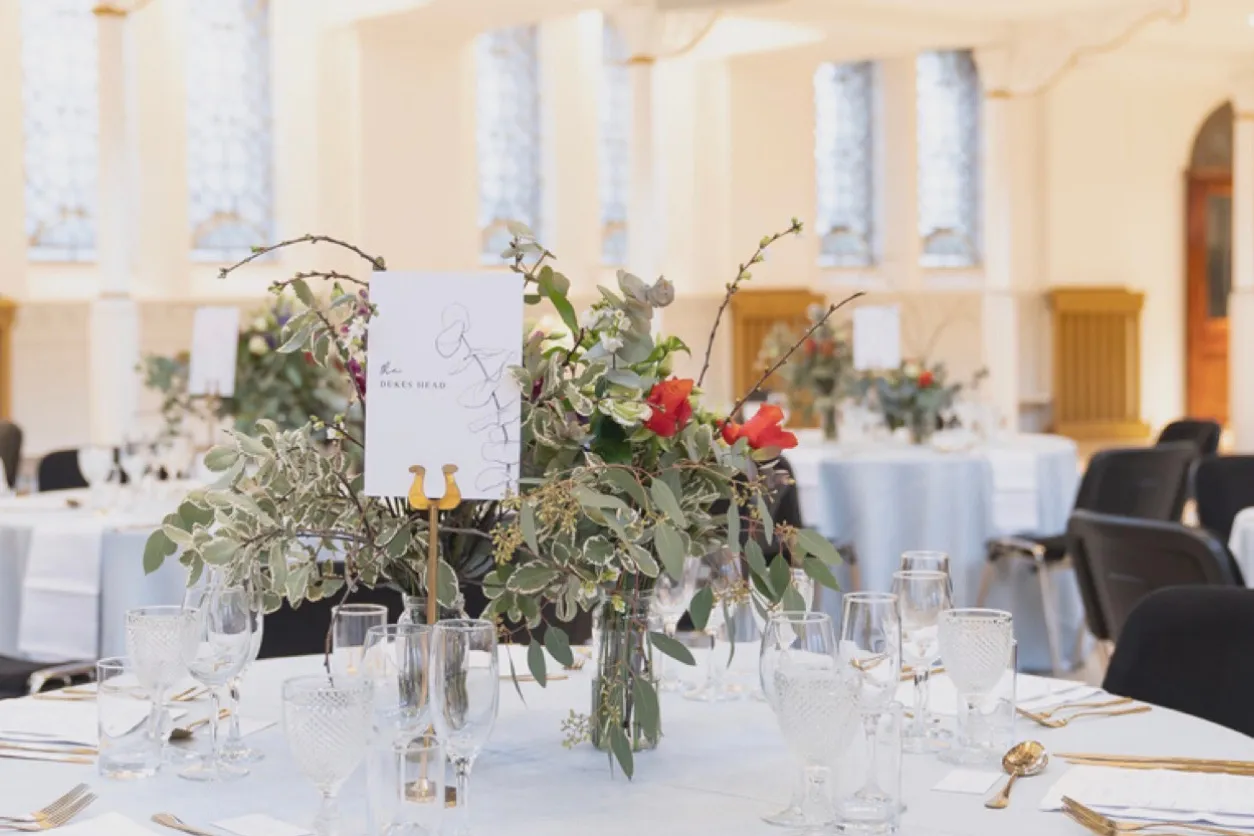 Round tables laid for a dinner beneath the lancet windows, flowers and glassware on pale linen