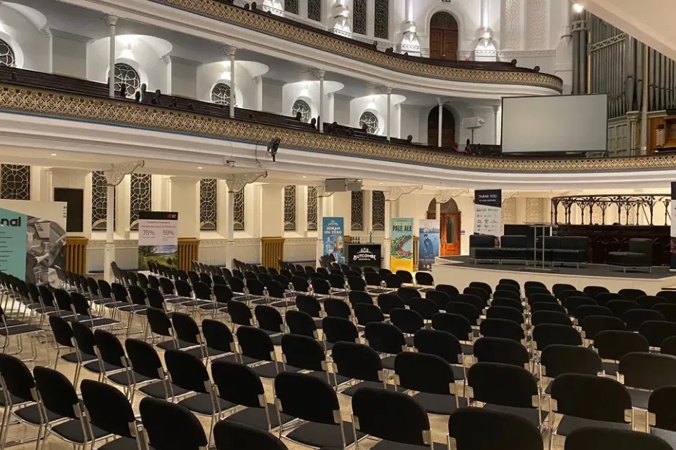 Rows of conference seating on the floor of the auditorium, exhibitor banners along the side and a stage at the front