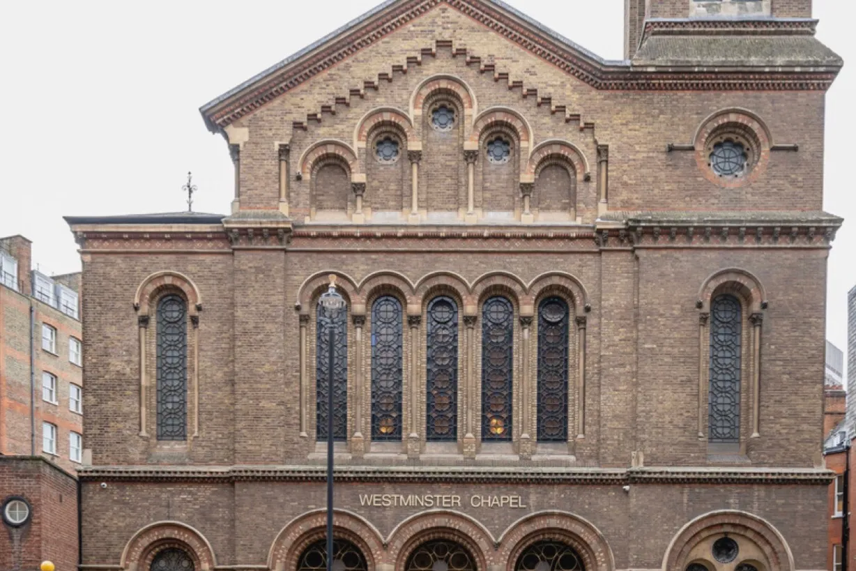 The brick frontage from across the street, arched windows above the entrance under a stepped gable