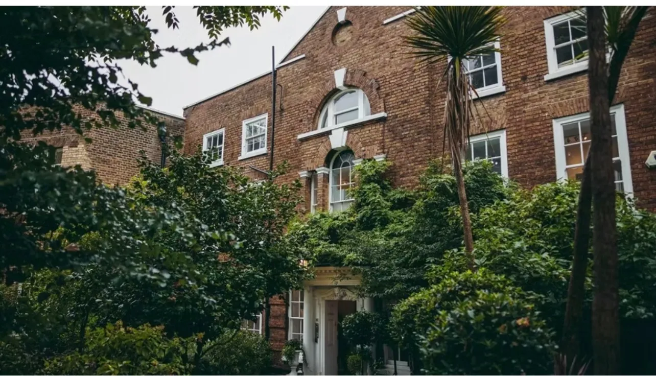 The frontage of one of the venues in OMB's care, sash windows and a fanlit doorway set behind trees