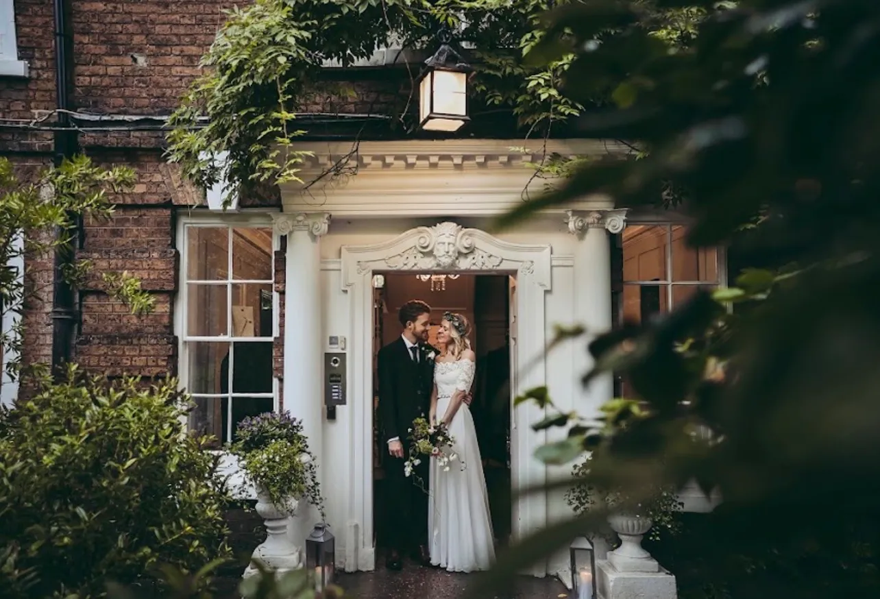 A couple in the pillared doorway, wisteria growing over the portico above them
